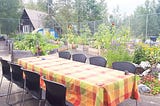 A picture of a table with chairs and a table cloth in a community garden ready to be set.