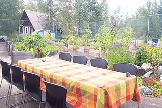 A picture of a table with chairs and a table cloth in a community garden ready to be set.